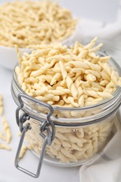 Uncooked trofie pasta in glass jar on white table, closeup
