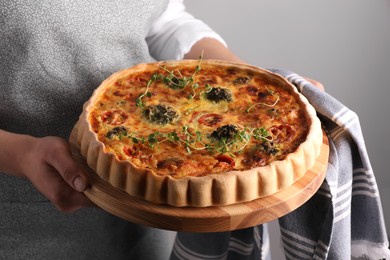 Woman holding delicious homemade vegetable quiche on light gray background, closeup