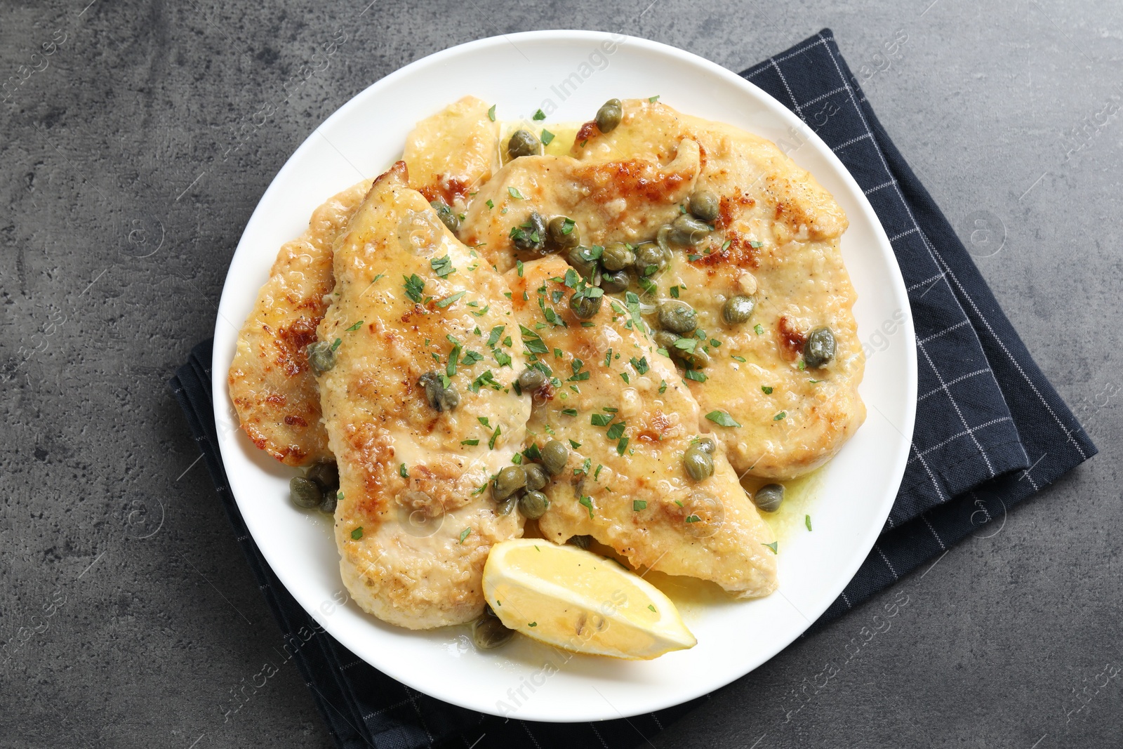 Photo of Delicious chicken piccata with herbs on grey table, top view