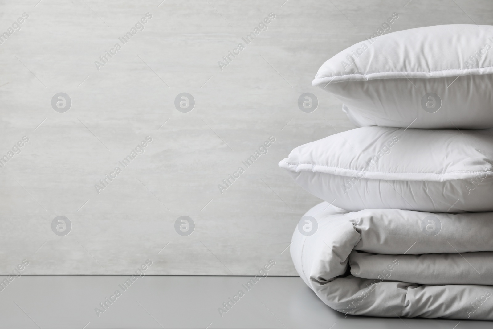 Photo of Soft folded blanket and pillows on light grey table, closeup. Space for text