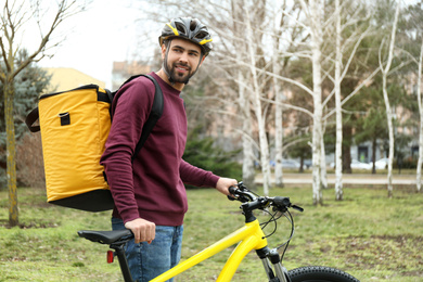 Photo of Courier with thermo bag and bicycle outdoors. Food delivery service