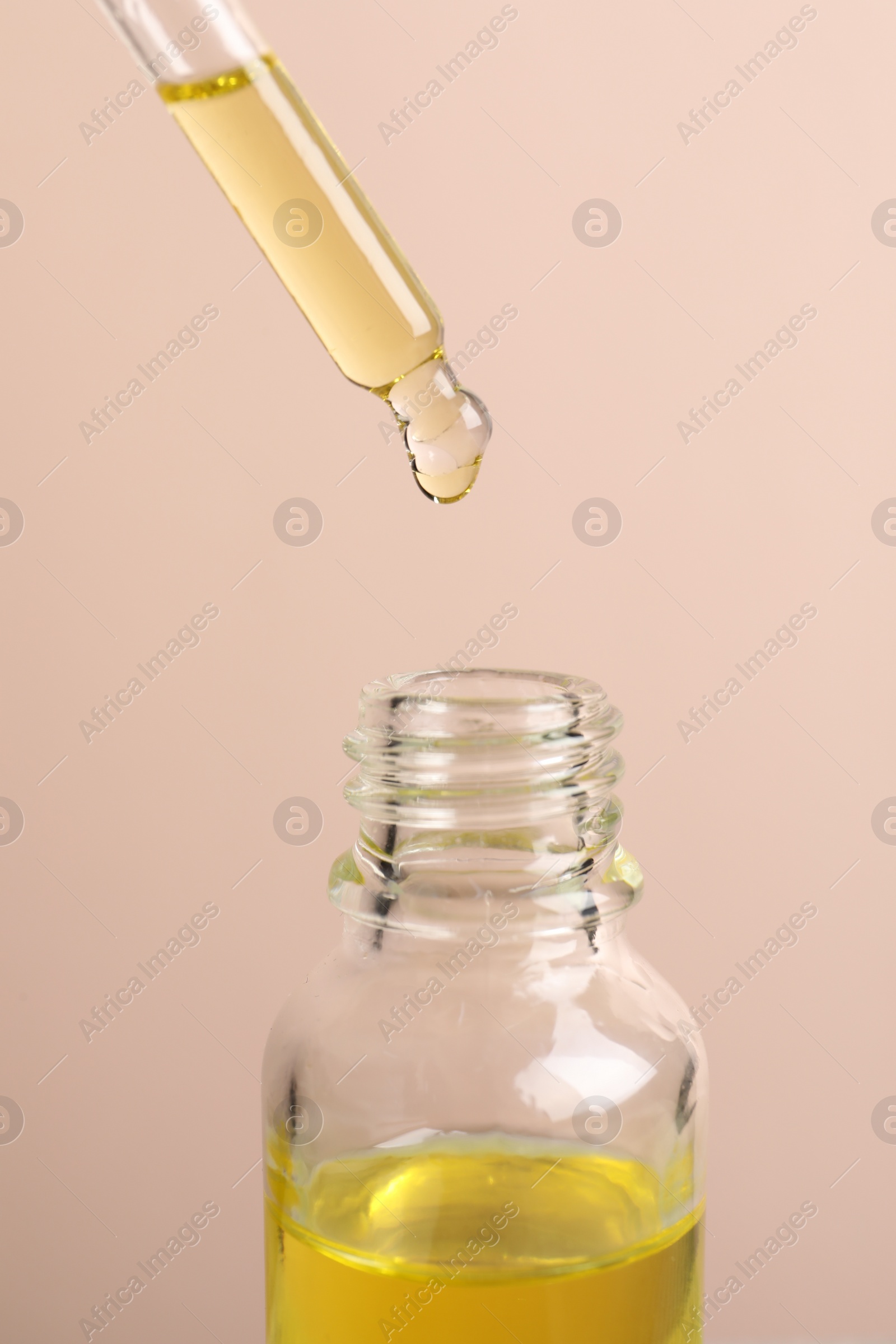 Photo of Dripping cosmetic serum from pipette into bottle on beige background