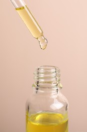 Dripping cosmetic serum from pipette into bottle on beige background