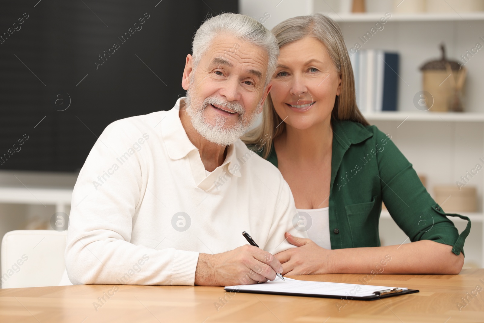 Photo of Happy senior couple signing Last Will and Testament indoors