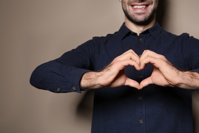 Man showing HEART gesture in sign language on color background, closeup