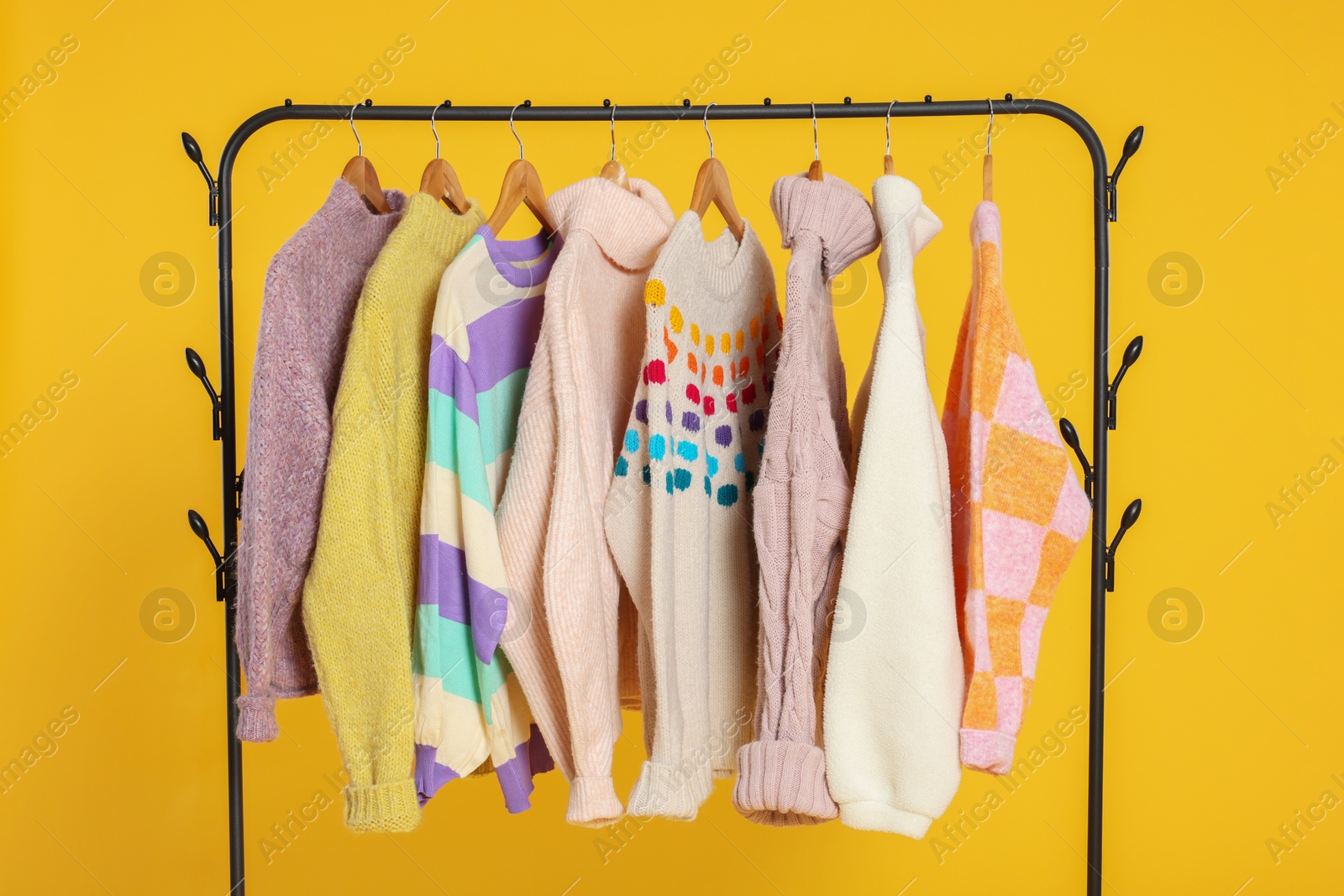 Photo of Rack with stylish women's sweaters on wooden hangers against orange background