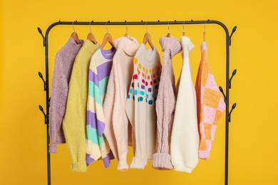 Photo of Rack with stylish women's sweaters on wooden hangers against orange background