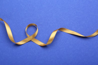 Photo of Beautiful golden ribbon on blue background, top view
