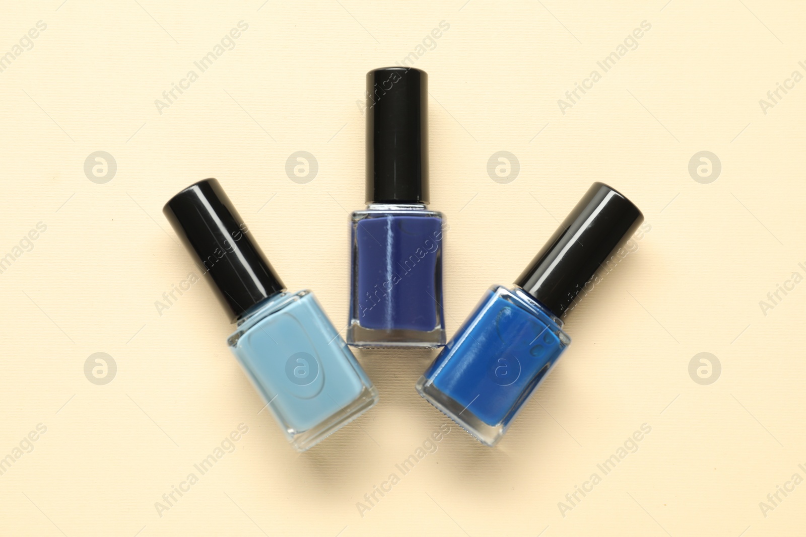 Photo of Bright nail polishes in bottles on beige background, flat lay