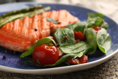 Photo of Tasty grilled salmon with tomatoes, spinach and spices on table, closeup