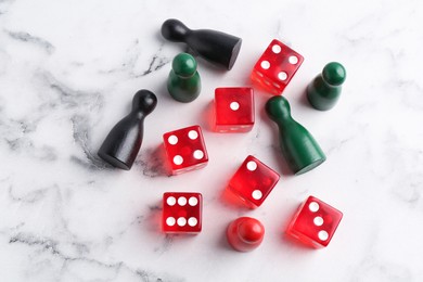 Red dices and game pieces on white marble table, flat lay