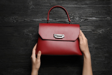 Photo of Woman holding small bag on black wooden background, top view