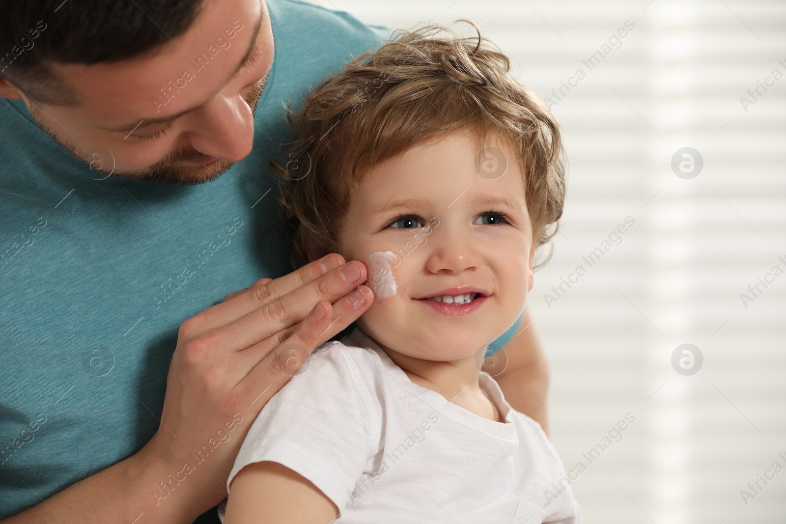 Photo of Father applying ointment onto his son`s cheek indoors