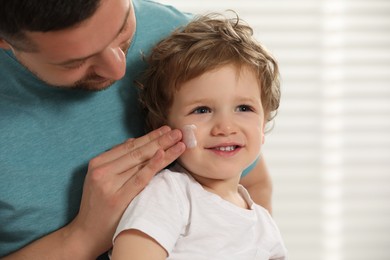 Father applying ointment onto his son`s cheek indoors