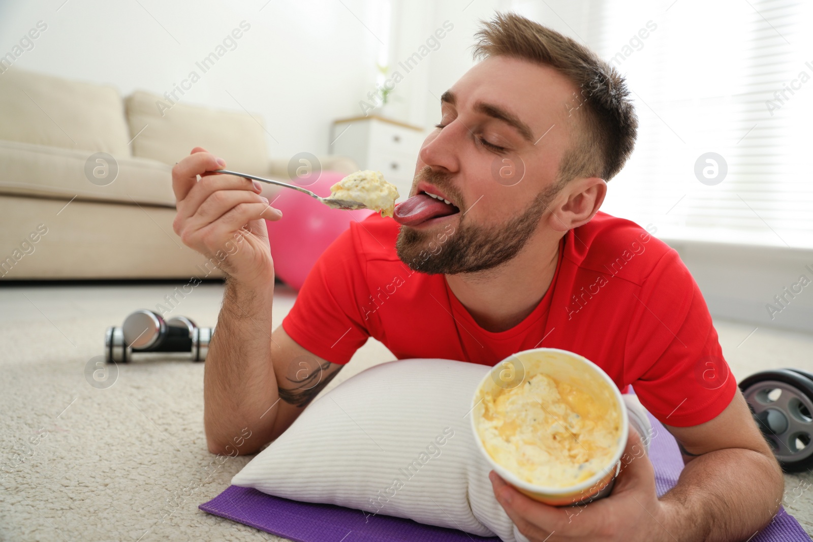 Photo of Lazy young man eating ice cream instead of training at home