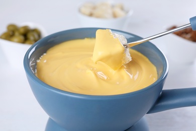 Dipping bread into pot with cheese fondue on table, closeup