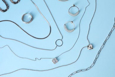 Metal chains and other different accessories on light blue background, flat lay. Luxury jewelry