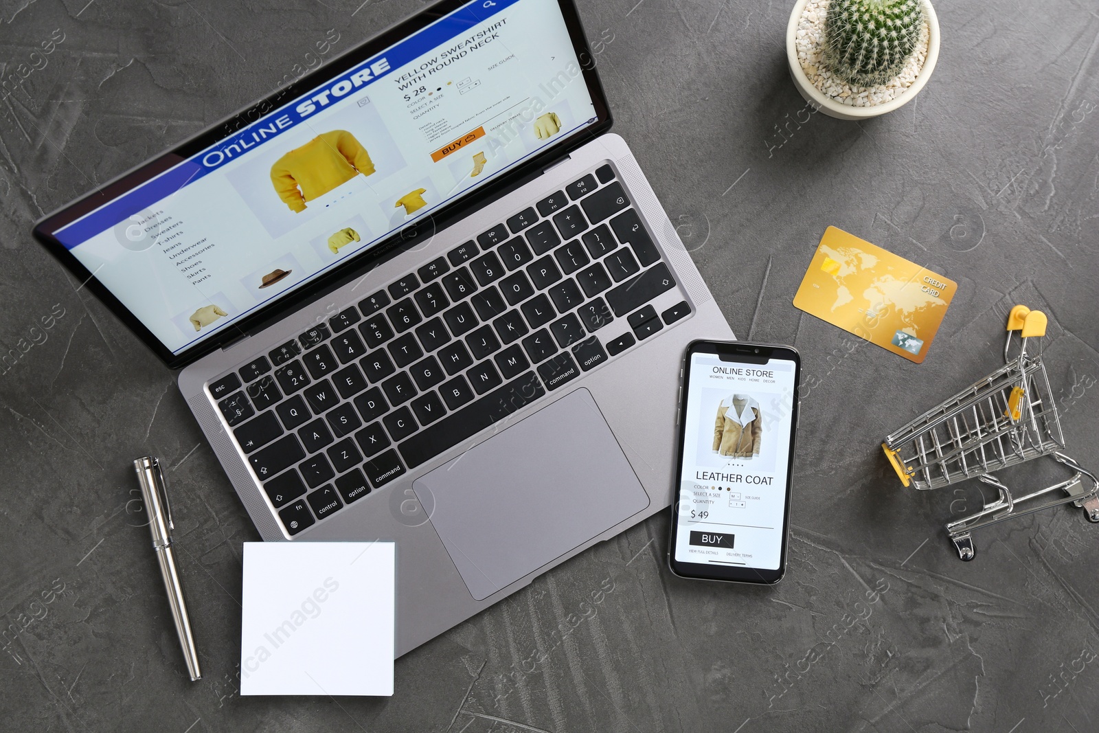 Photo of Online store website on laptop screen. Computer, smartphone, credit card, stationery, shopping cart and cactus on grey table, flat lay