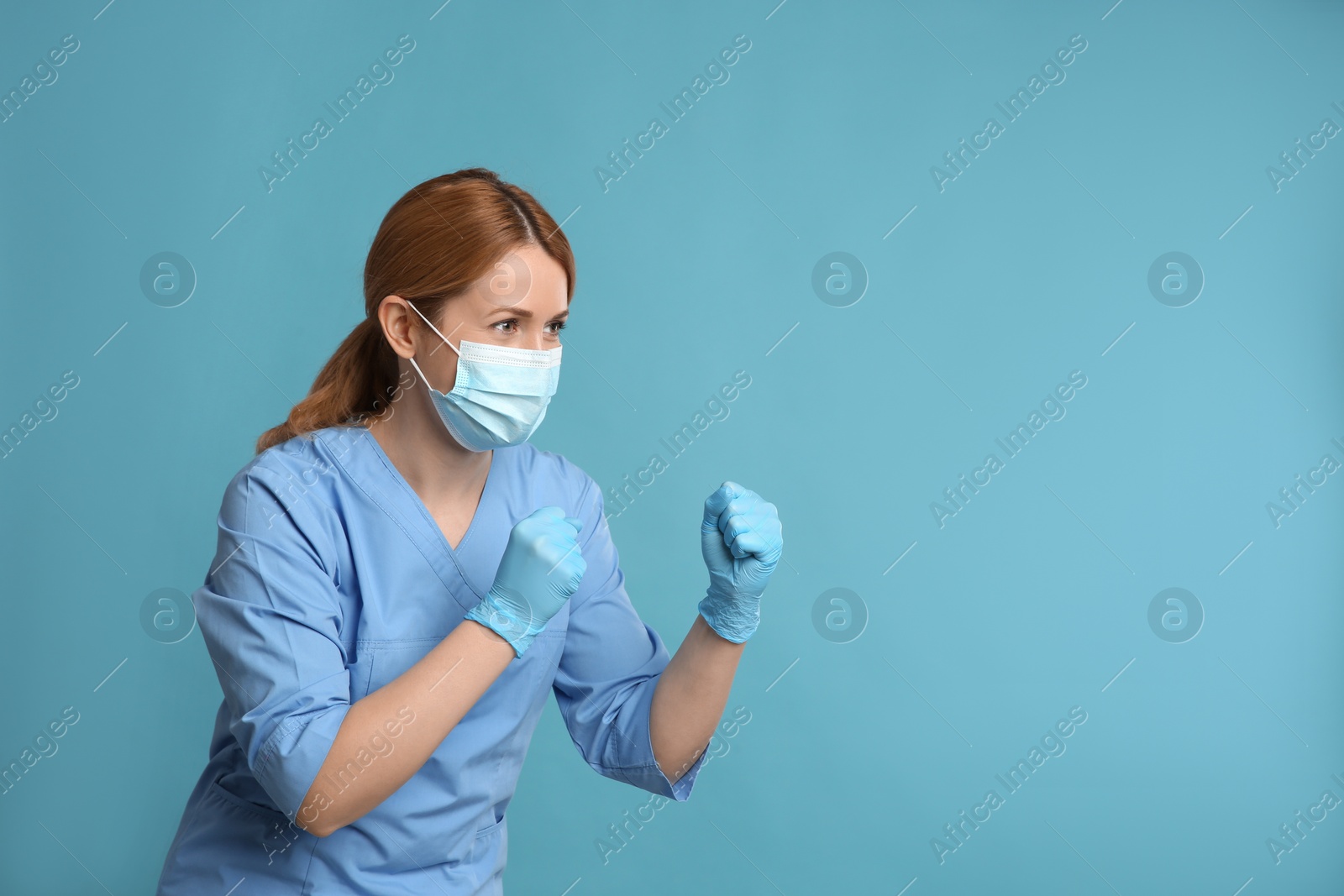 Photo of Doctor with protective mask in fighting pose on light blue background, space for text. Strong immunity concept