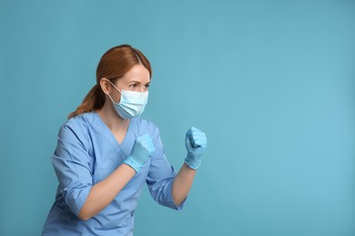 Doctor with protective mask in fighting pose on light blue background, space for text. Strong immunity concept