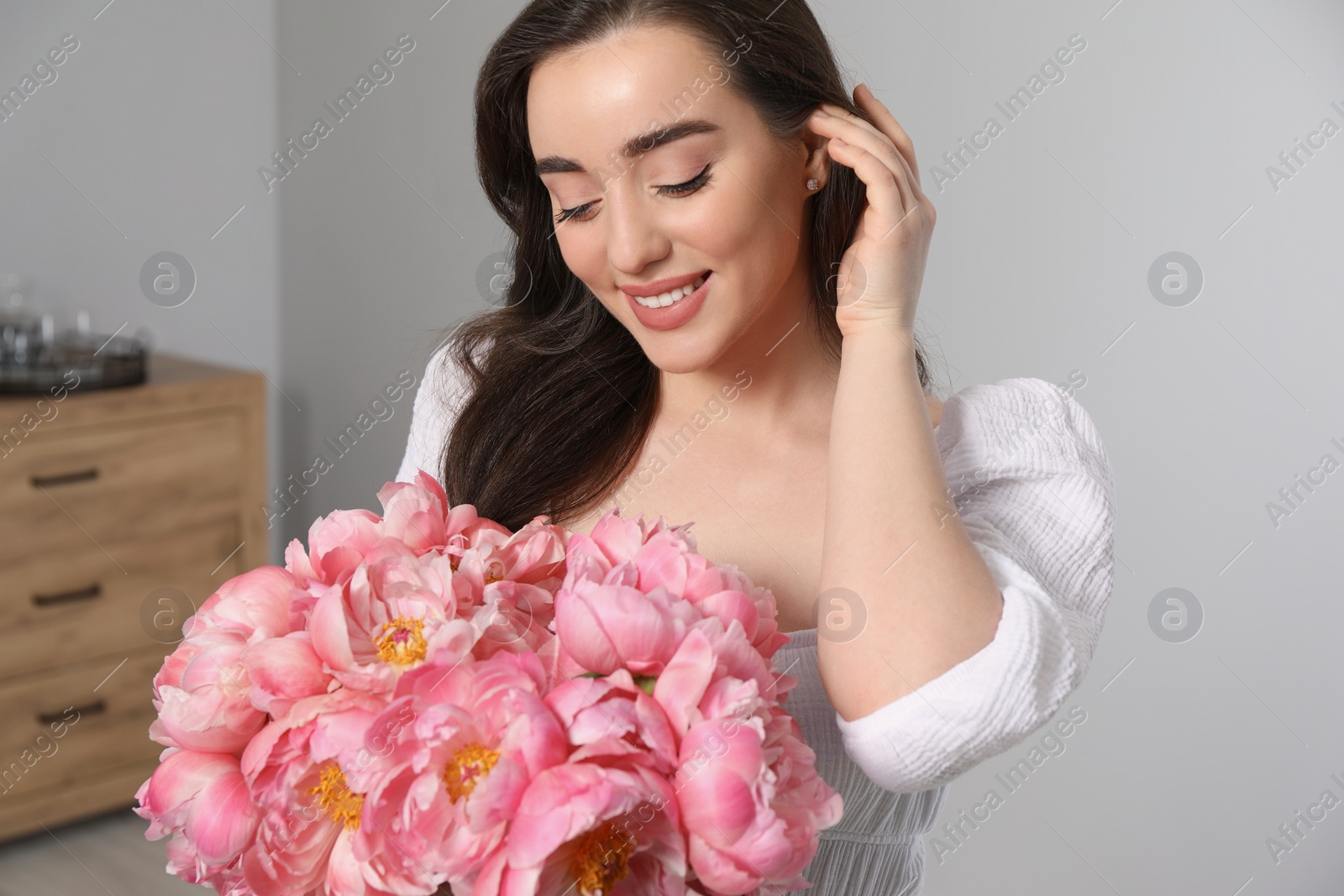 Photo of Beautiful young woman with bouquet of pink peonies at home