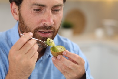 Man eating kiwi with spoon on blurred background, closeup. Space for text