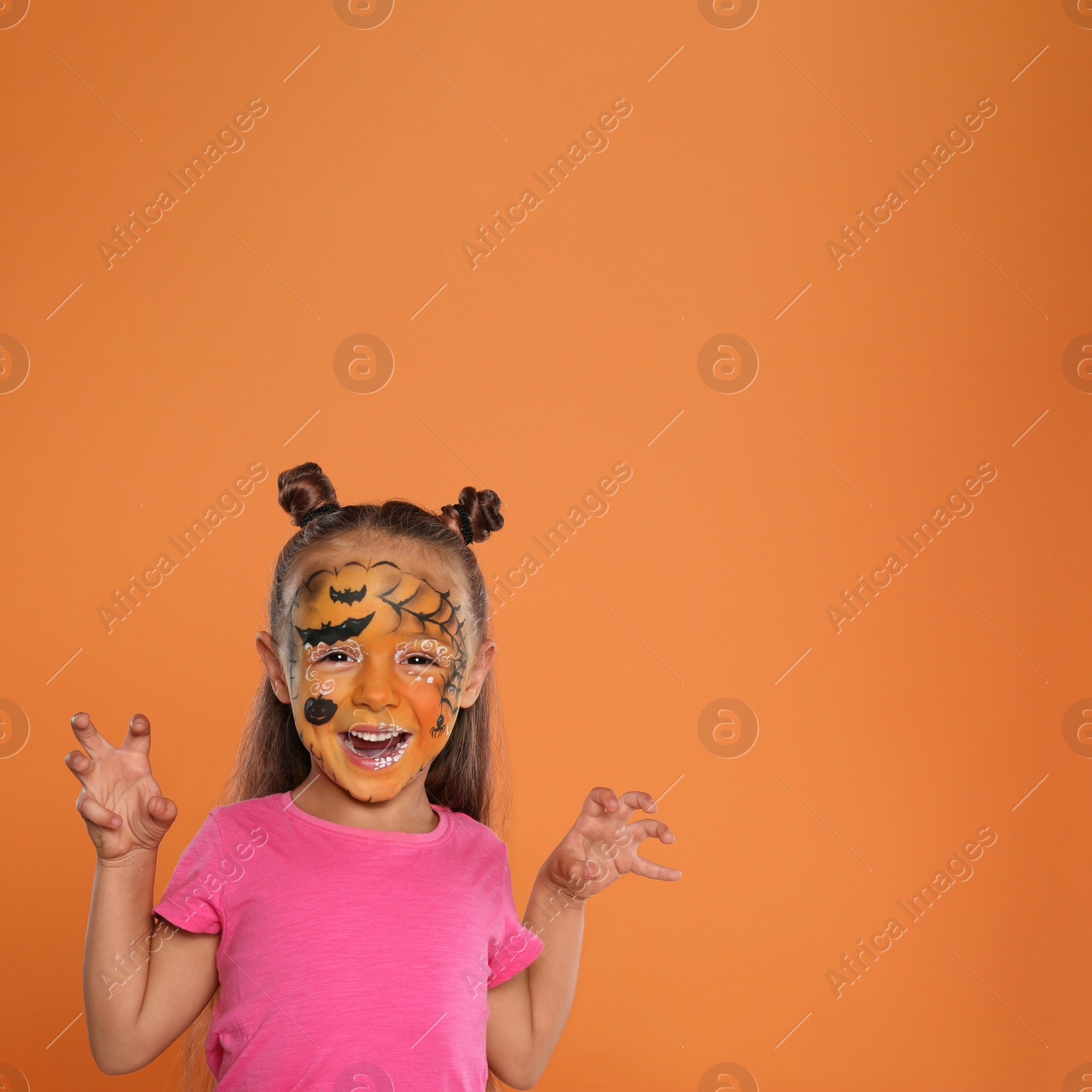 Photo of Cute little girl with face painting on orange background. Space for text