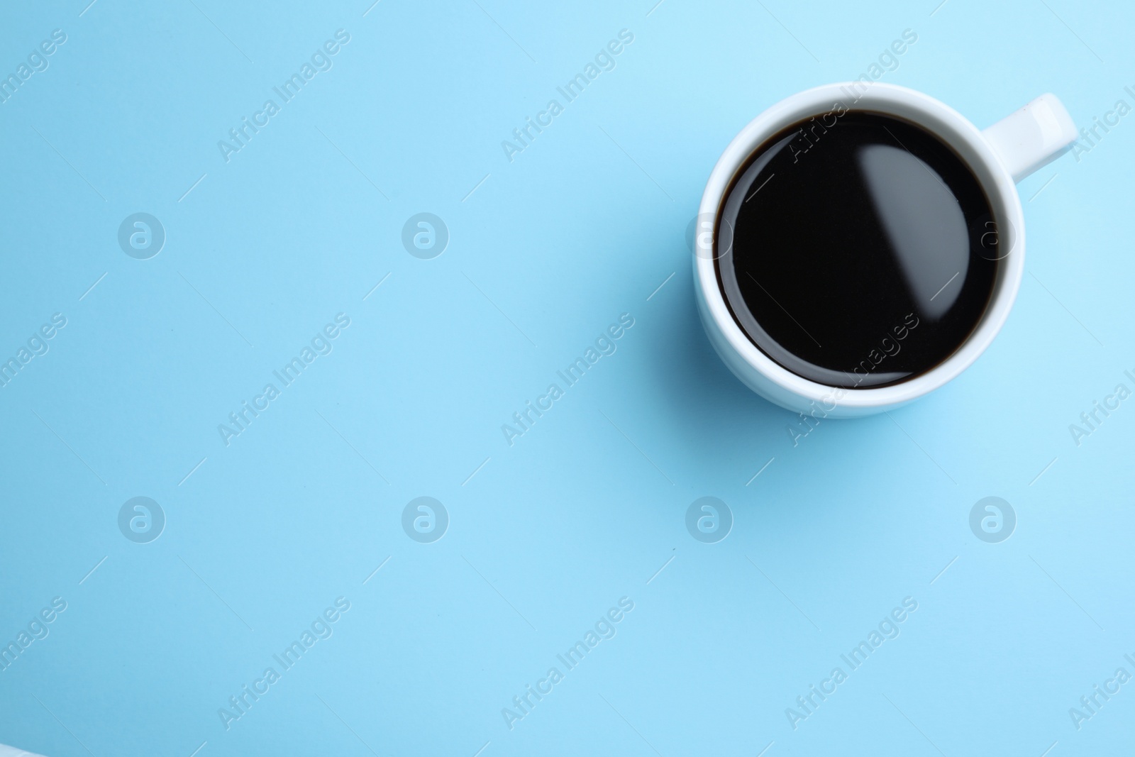 Photo of White mug of freshly brewed hot coffee on light blue background, top view. Space for text