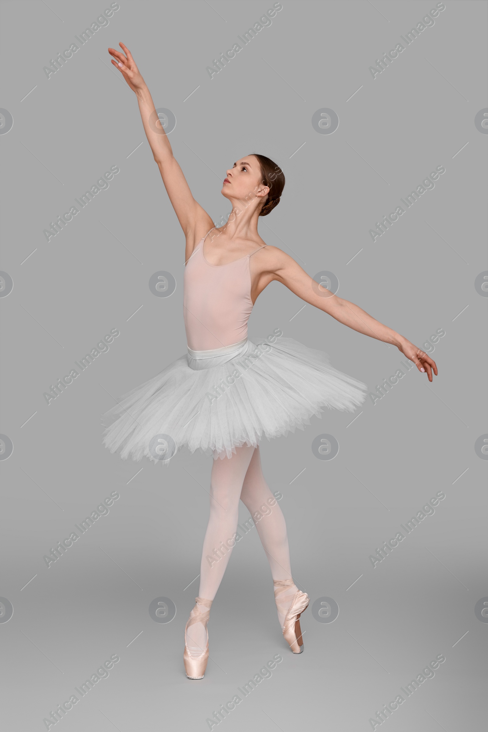 Photo of Young ballerina practicing dance moves on light grey background
