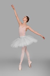 Photo of Young ballerina practicing dance moves on light grey background