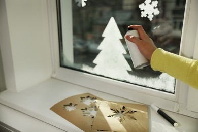 Woman using snow spray for decorating window at home, closeup