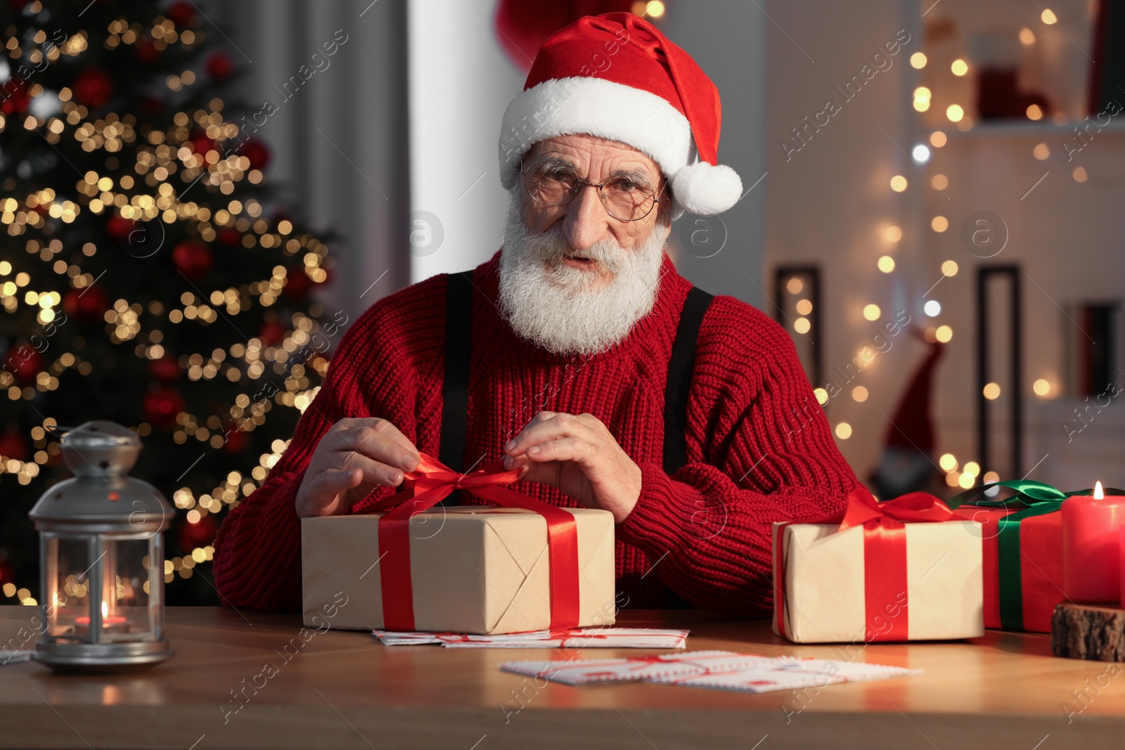 Photo of Santa Claus with Christmas gift at his workplace in decorated room