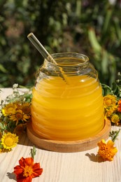 Taking delicious fresh honey with dipper from glass jar surrounded by beautiful flowers on table in garden