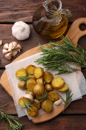 Delicious baked potatoes with rosemary and garlic on wooden table, flat lay