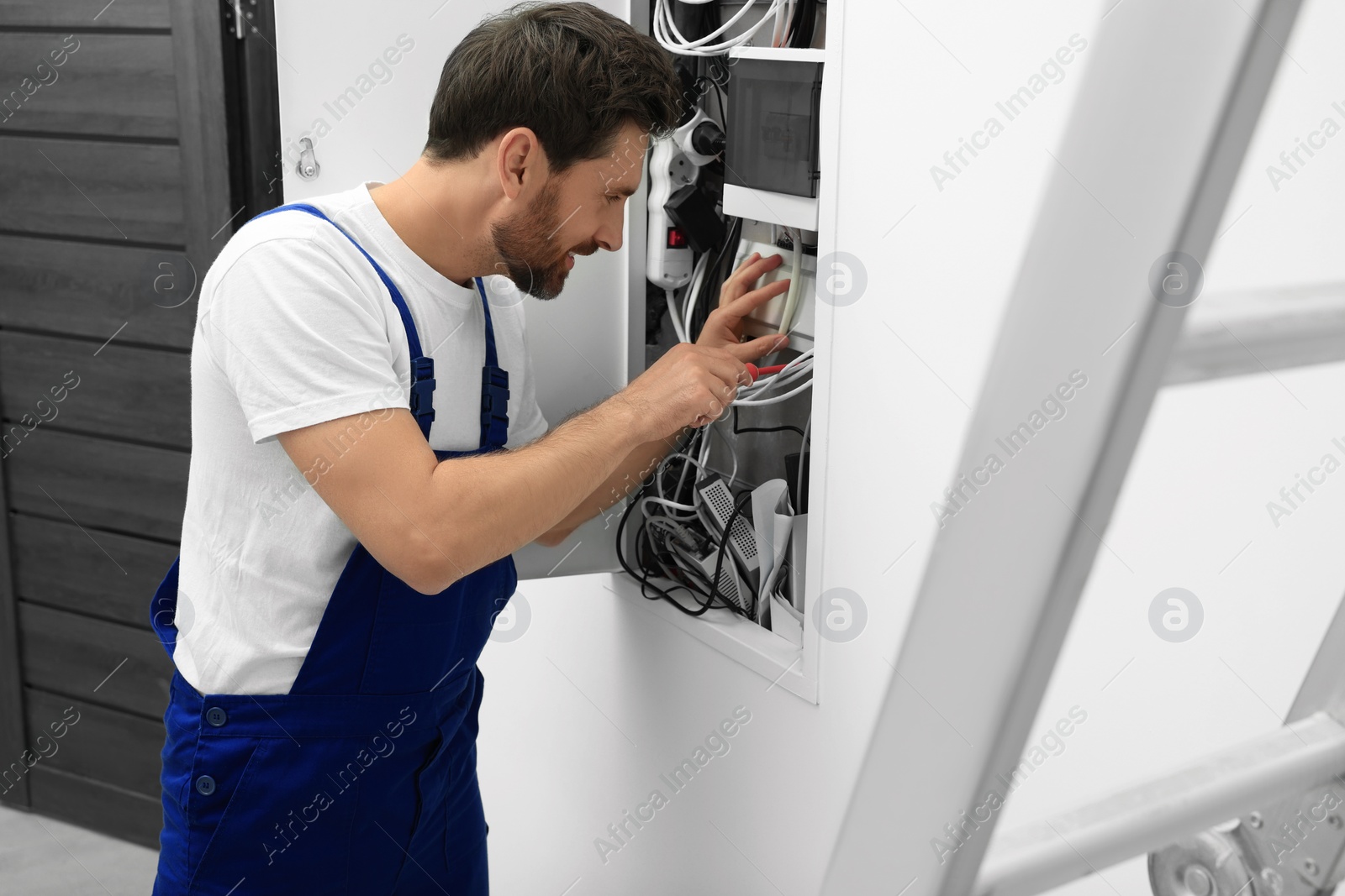 Photo of Electrician repairing fuse box with screwdriver indoors