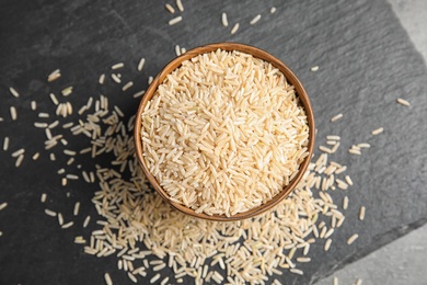 Photo of Slate plate with raw unpolished rice in bowl on table, top view