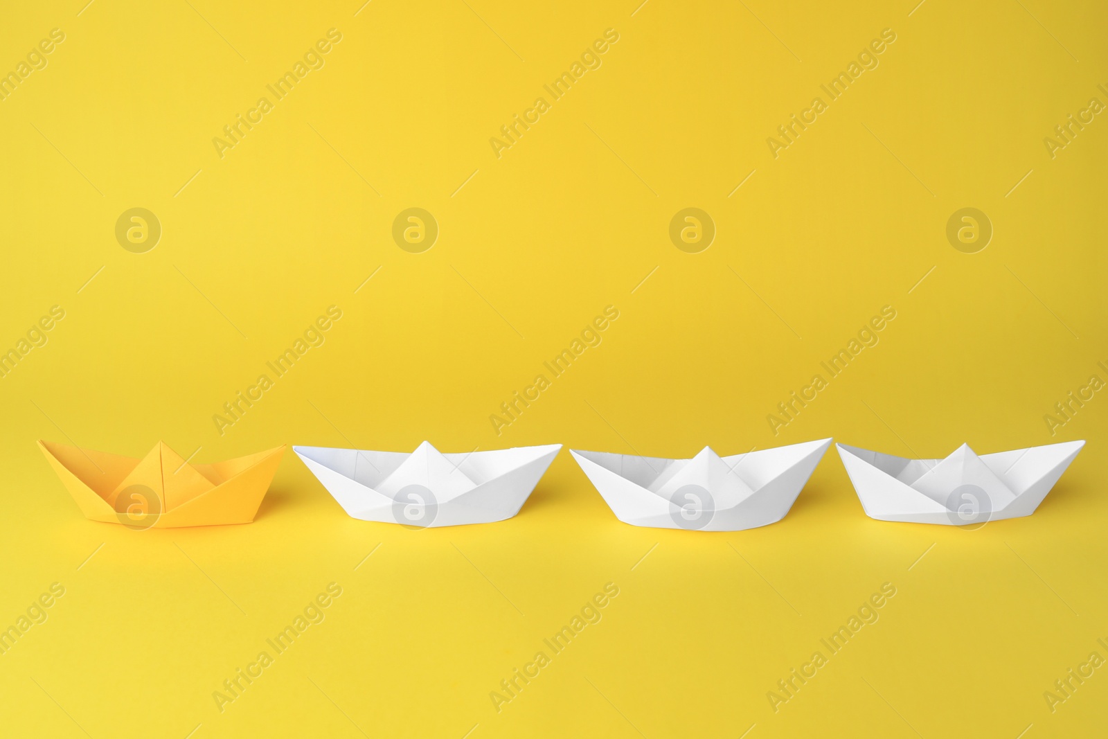 Photo of Group of paper boats following yellow one on color background. Leadership concept