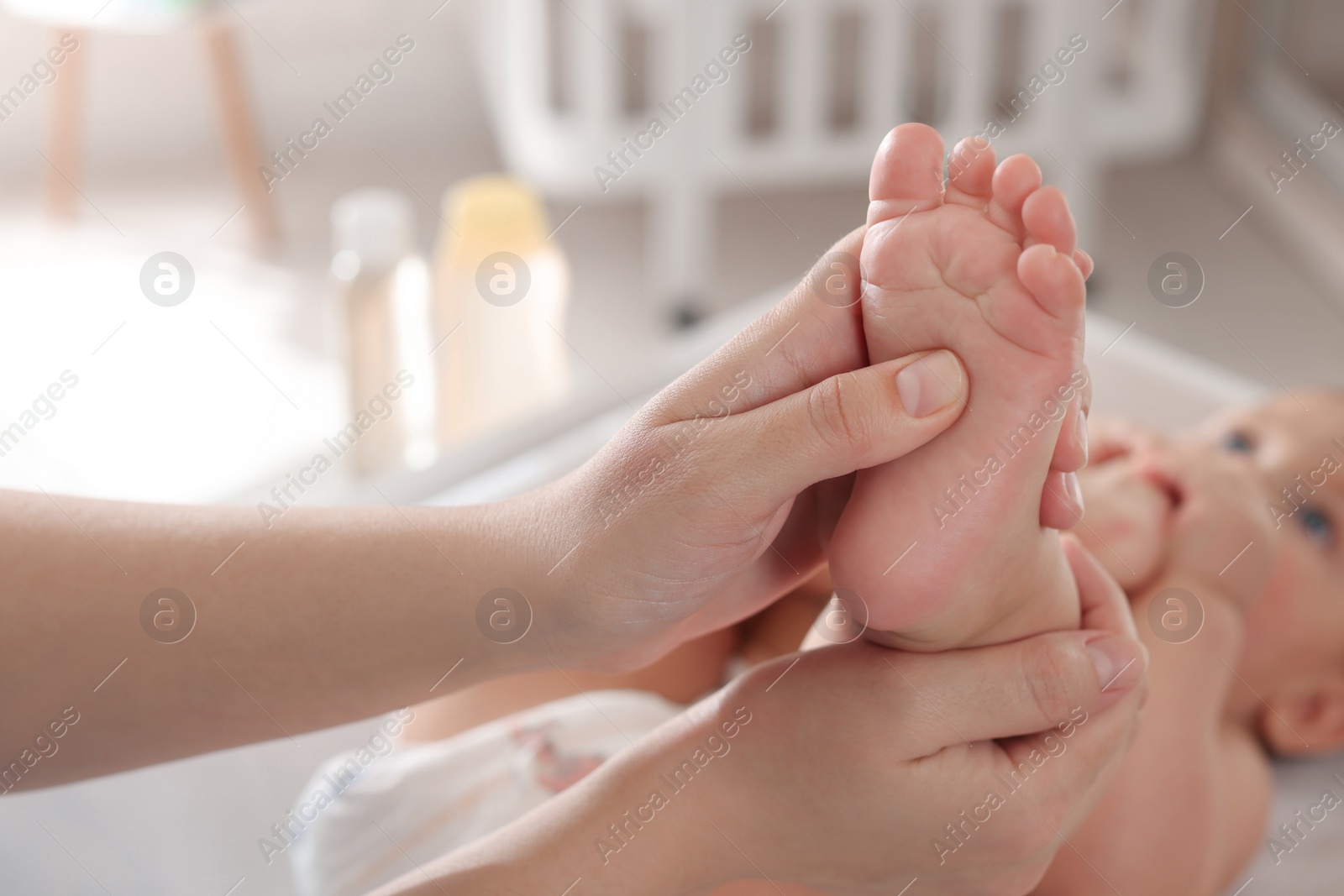 Photo of Mother massaging her baby with oil on changing table at home, closeup