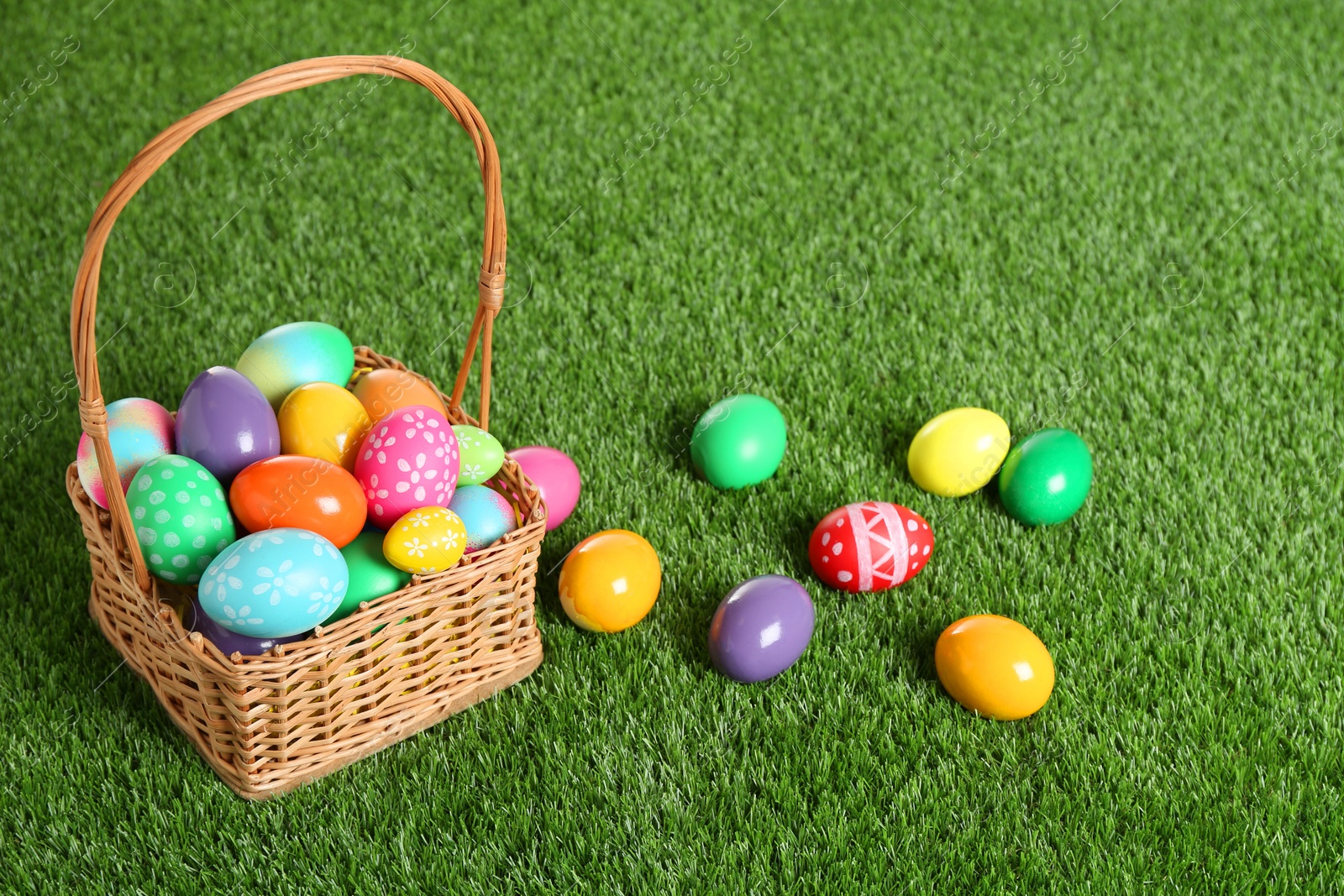 Photo of Wicker basket with Easter eggs on green grass. Space for text