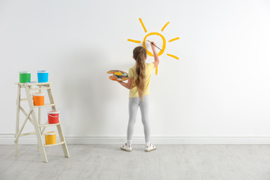 Little child painting sun on white wall indoors