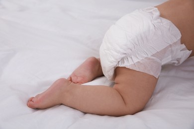 Photo of Cute baby in dry soft diaper on white bed, closeup