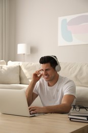 Photo of Man with laptop and headphones at table indoors