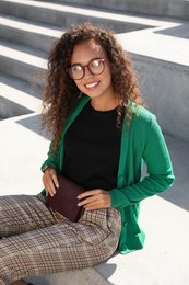 Photo of Beautiful African American woman with stylish waist bag on stairs outdoors