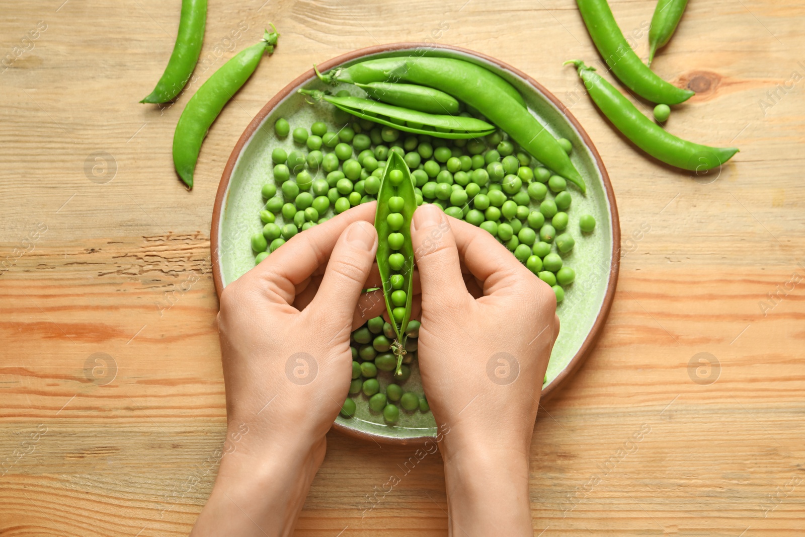 Photo of Woman shelling green peas over table, top view