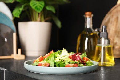 Plate of salad and bottles with cooking oil on black table in kitchen