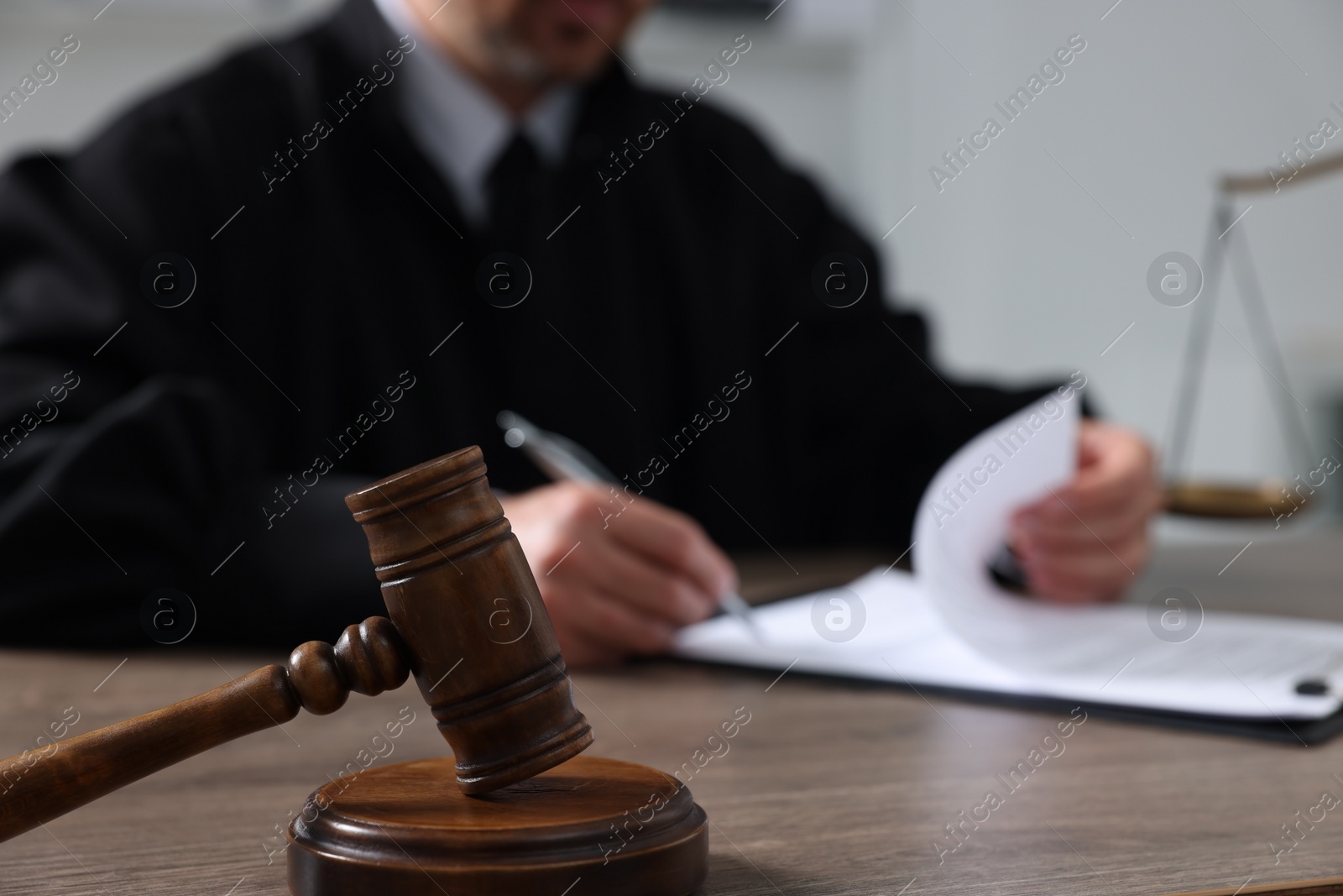 Photo of Judge with gavel writing in papers at wooden table indoors, closeup