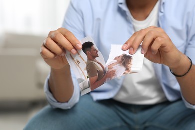 Photo of Man tearing photo indoors, closeup. Divorce concept