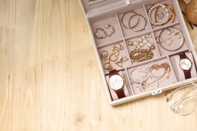 Jewelry box with many different accessories on light wooden table, flat lay. Space for text