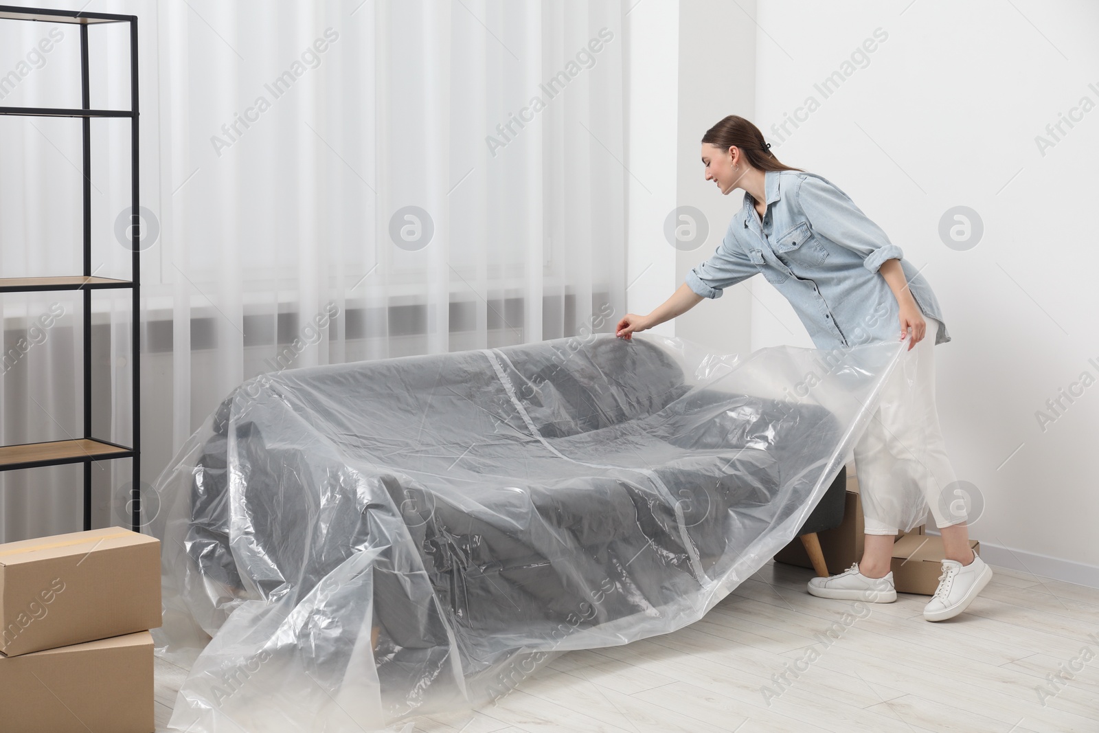 Photo of Young woman putting plastic film away from sofa at home