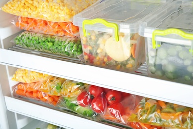 Photo of Containers and plastic bags with deep frozen vegetables in refrigerator